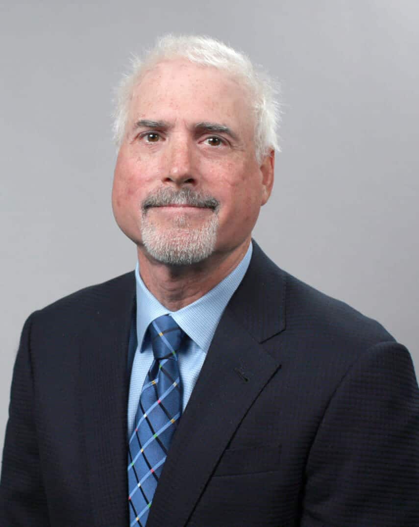 headshot of man in suit and tie confidently smiling against solid off-white background