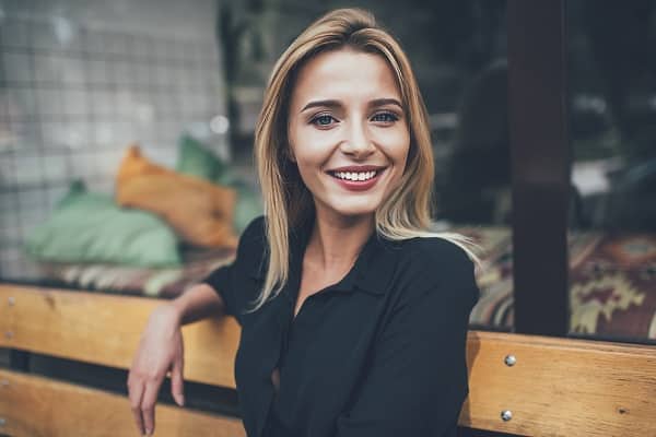 Close up portrait of a young Millennial woman with blonde hair and a black blouse seated on a bench