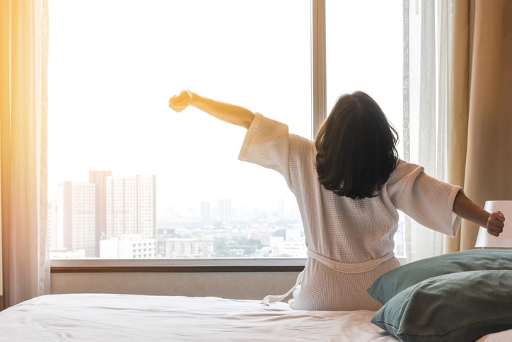 Woman sitting at the edge of her bed stretching her arms.