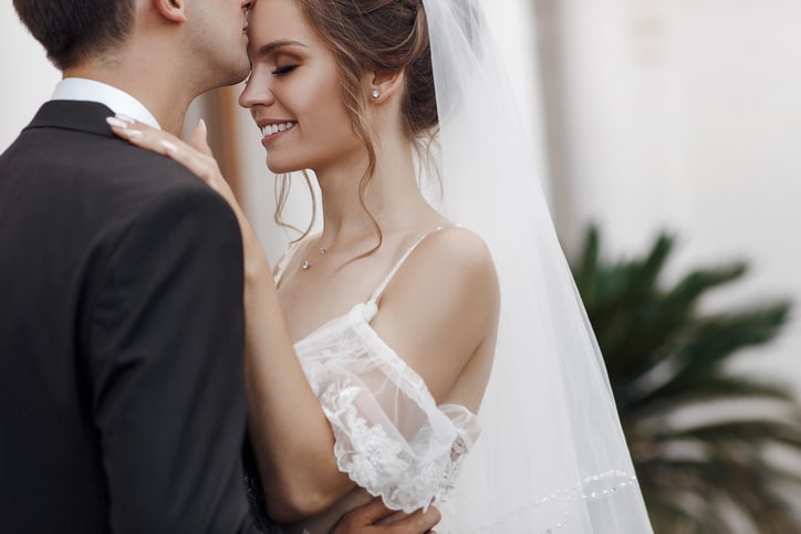 Close up image of a bridge being kissed on the forehead by her groom