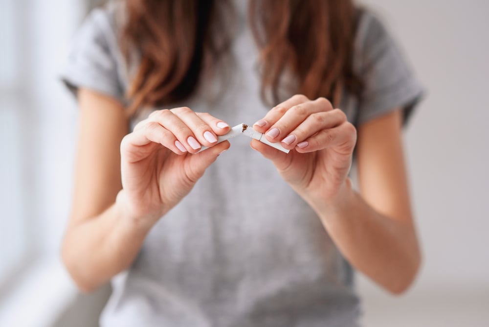 A close up of a woman in a gray shirt breaking a cigarette in half