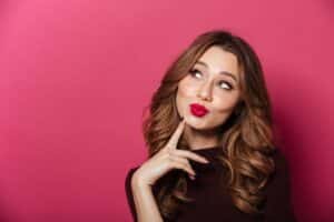 Young woman with smooth skin and playful expression against a pink background, representing the subtle results of Baby Botox.