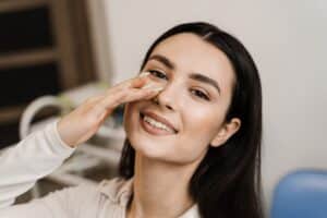 Woman smiling and gently touching her nose, representing personalized rhinoplasty and natural-looking facial harmony.
